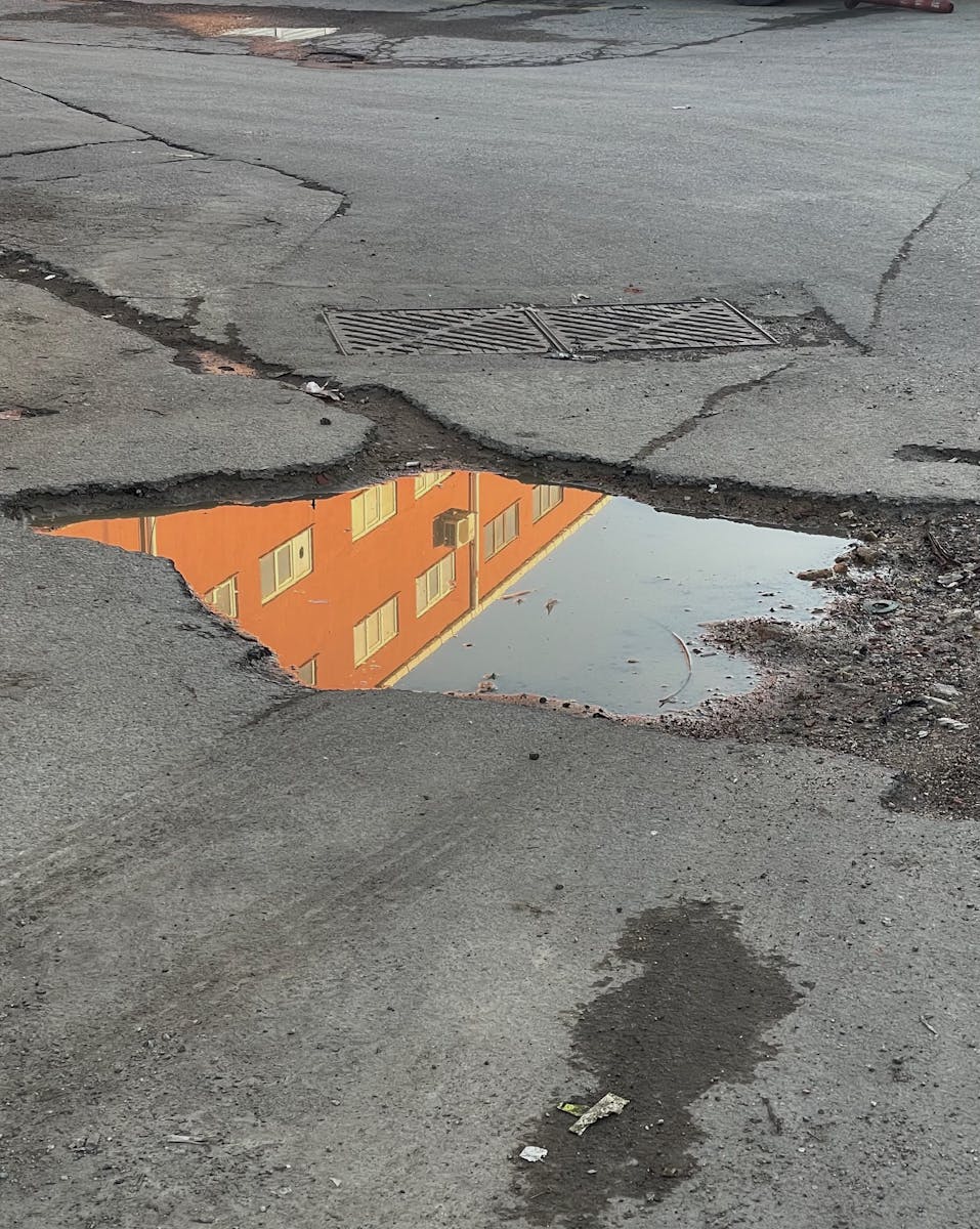 Urban street puddle reflecting orange building. Grungy city street scene with cracks and textures.